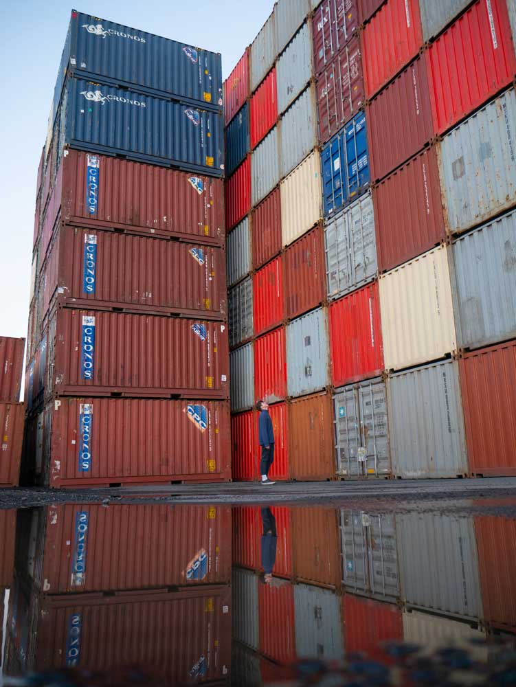 A young man looks up at stacked shipping containers, used by ocean freight services to move large amounts of cargo.