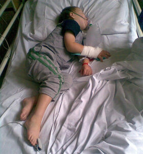 A sick child lying in a hospital bed wearing an oxygen mask