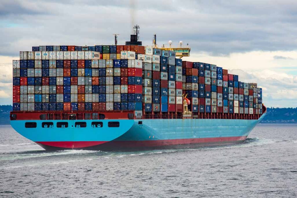 A red and blue cargo ship on sea carrying countless intermodal containers