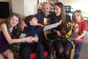 A happy family with three children celebrating a birthday with a chocolate cake in the mother's hand